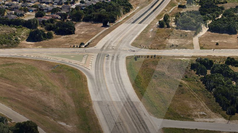 aerial photo of two roads intersecting with a neighborhood in one corner and open land around